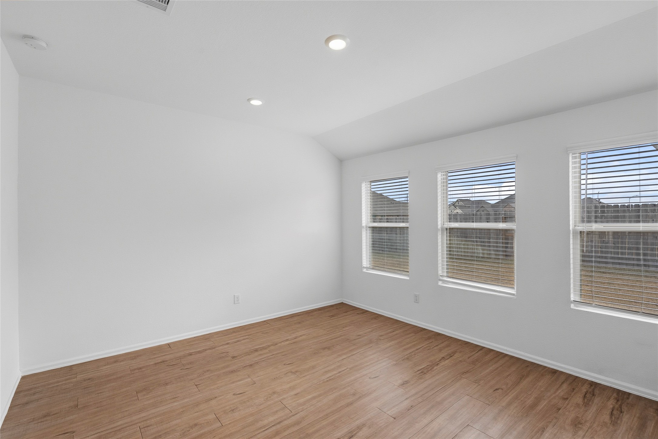 3705 Paloma Fls Lane Rosenberg, TX 77469 - Photo 22 of 27 Spacious fourth bedroom with a vaulted ceiling, recessed lighting, and three backyard-facing windows with blinds. Warm-toned plank flooring and a clean, open wall create an easy layout for a bed or desk setup.