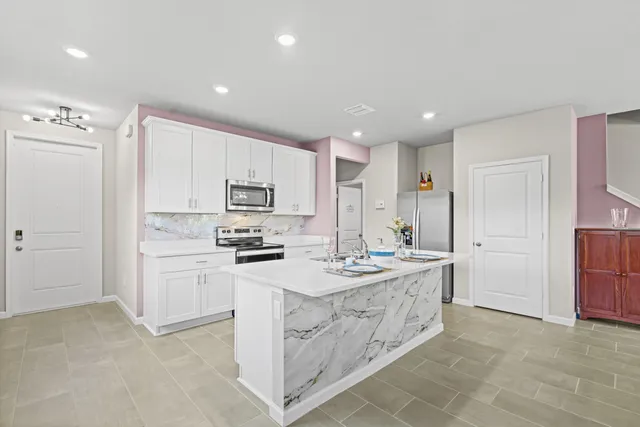 a kitchen that has a lot of white cabinets and stainless steel appliances