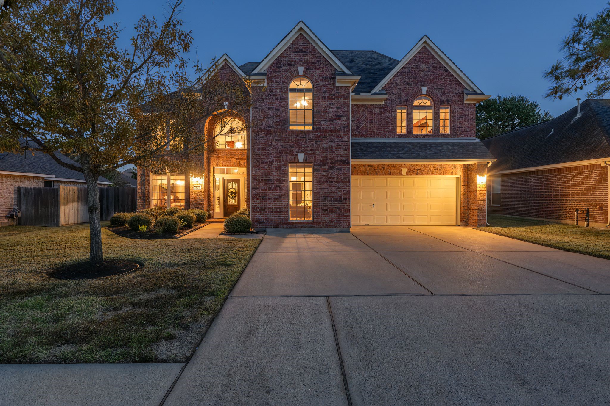 This inviting two-story brick home features a well-lit façade with large windows and a welcoming front entrance.