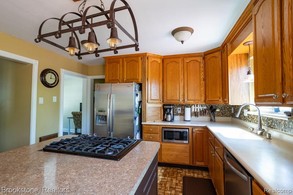 30100 Armada Ridge Road Richmond, MI 48062 - Photo 7 of 29 Kitchen featuring a center island with a built-in cooktop, stainless steel refrigerator, wood cabinetry, mosaic tile backsplash, and a contemporary ceiling light fixture