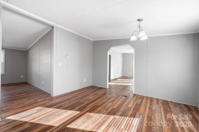 a view of empty room with wooden floor and chandelier