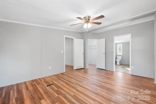 a view of an empty room with wooden floor and a ceiling fan