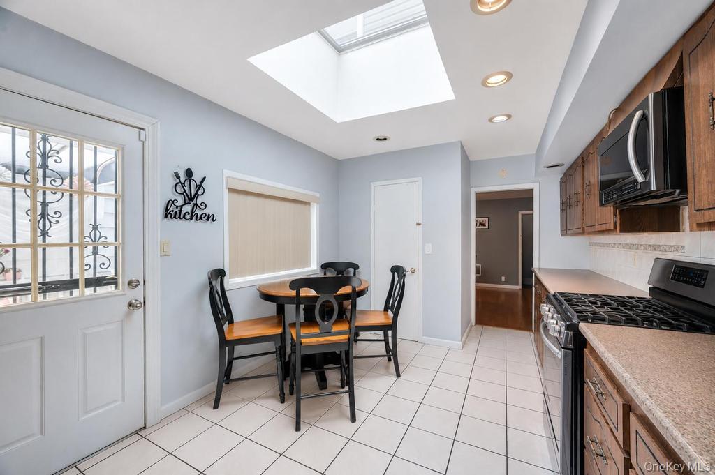 89-13 84th Street Queens, NY 11421 - Photo 19 of 34 Kitchen featuring white tile flooring, wooden cabinetry, stainless steel oven, recessed lighting, and a skylight