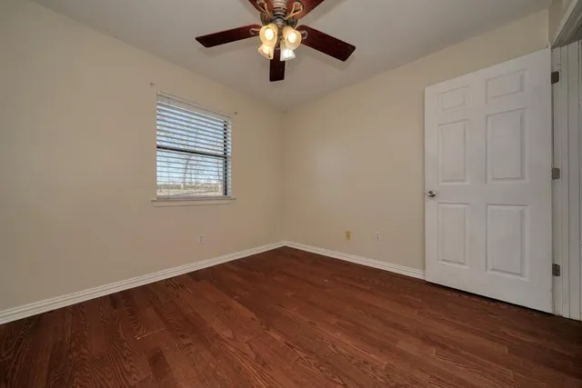 an empty room with wooden floor ceiling fan and windows