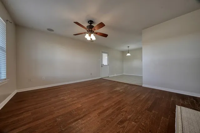 an empty room with wooden floor fan and windows