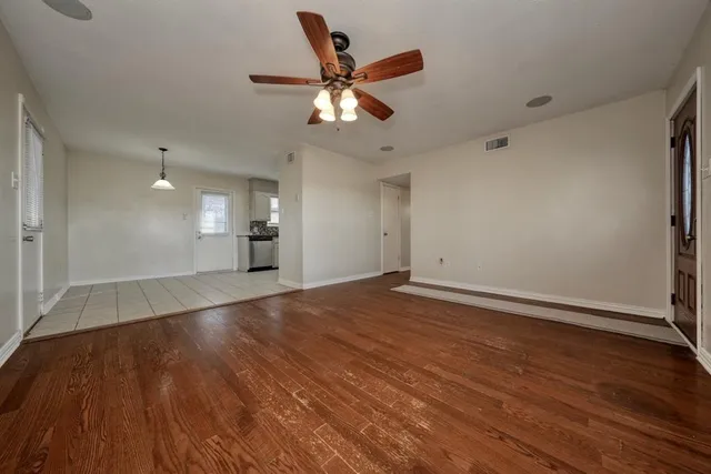 a view of an empty room with wooden floor and a ceiling fan