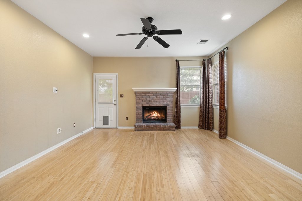 347 Spring Drive Kyle, TX 78640 - Photo 21 of 40 A comfortable living area, illuminated by natural light, features beautiful wood flooring and a cozy fireplace, perfect for relaxation.