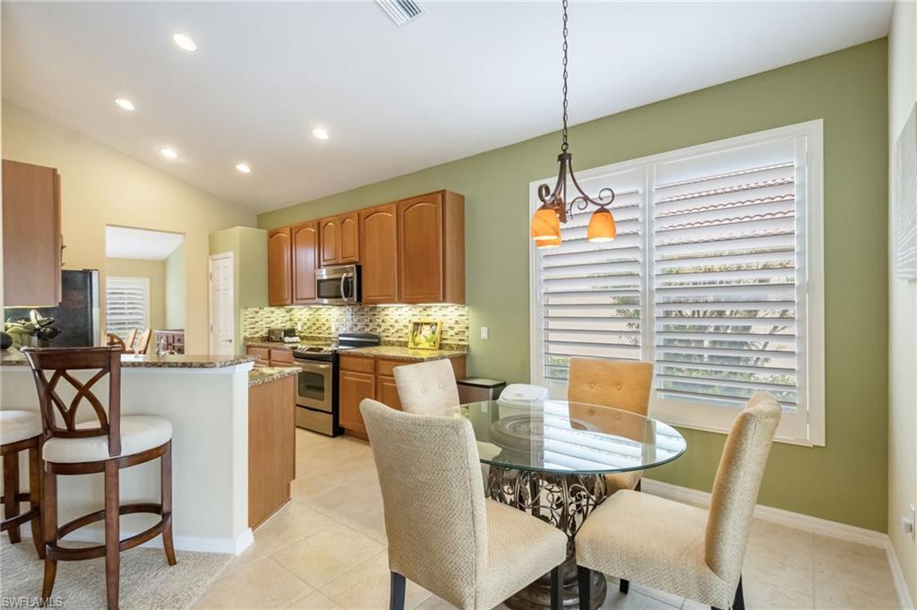 5857 Constitution Street Ave Maria, FL 34142 - Photo 10 of 40 a kitchen with stainless steel appliances kitchen island granite countertop a stove a refrigerator a kitchen island with chairs and white cabinets