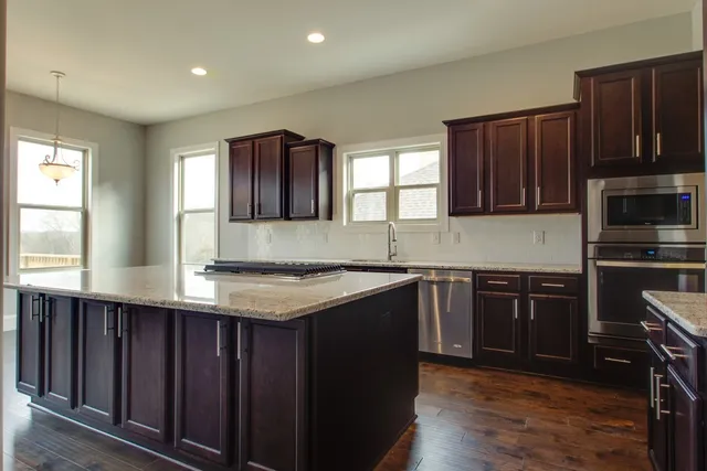 a kitchen with stainless steel appliances granite countertop wooden cabinets a stove a sink and dishwasher with wooden floor