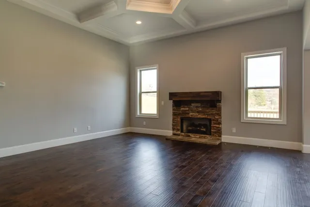 an empty room with wooden floor fire place and windows