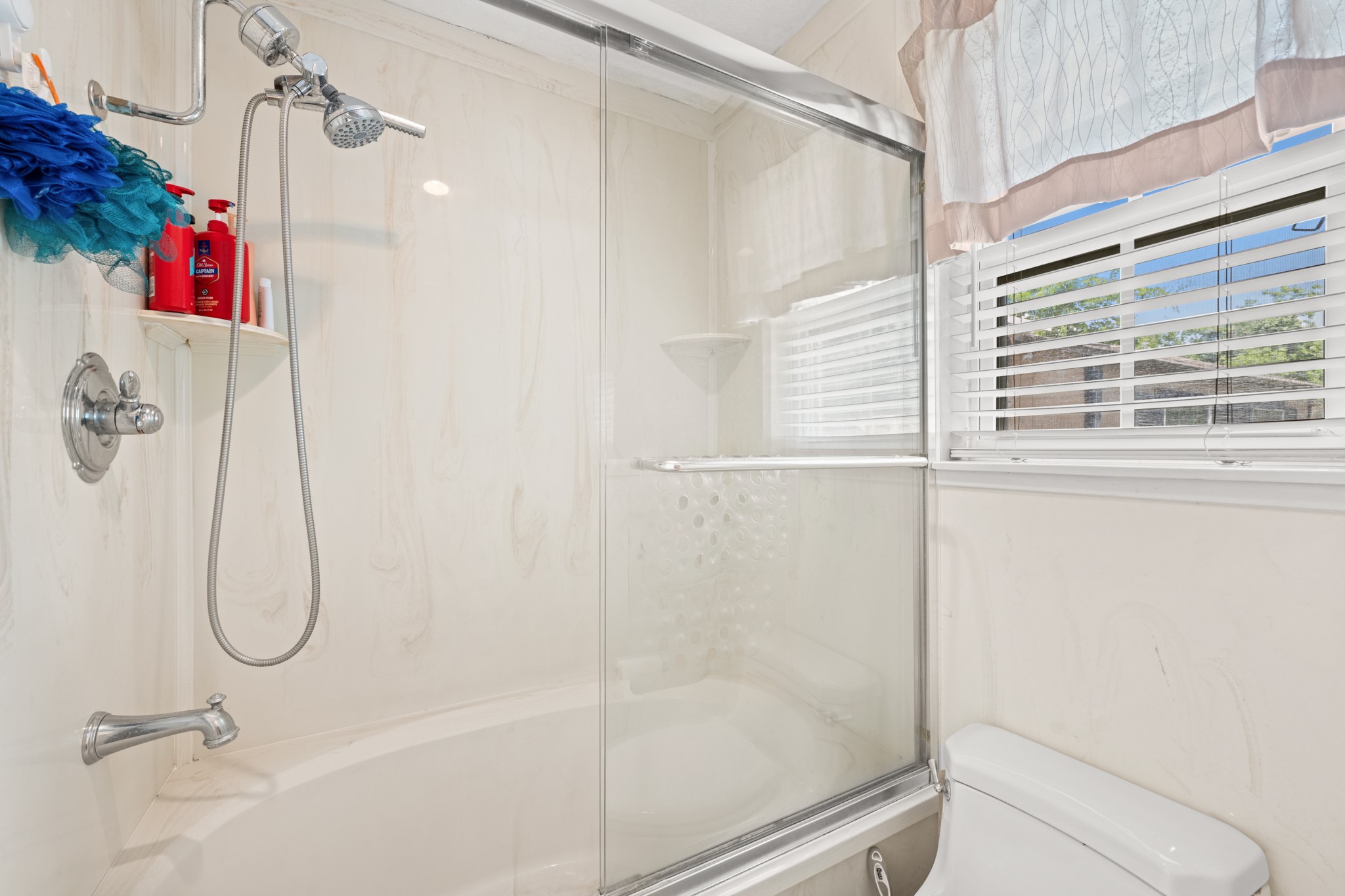 15602 Fir Road Santa Fe, TX 77517 - Photo 20 of 42 Bright primary bathroom featuring a tub/shower combination with glass enclosure and natural light from the nearby window. Clean finishes and a functional layout create a comfortable and practical everyday space.