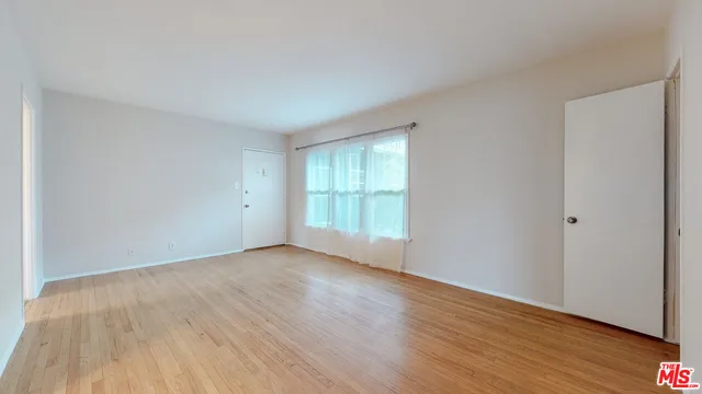a view of an empty room with wooden floor and a window