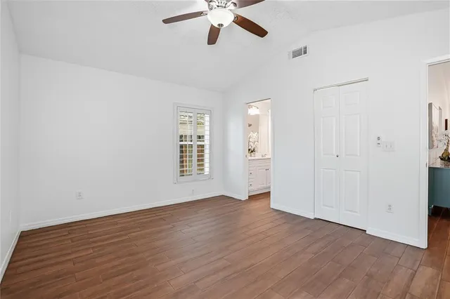 an empty room with wooden floor chandelier fan and windows