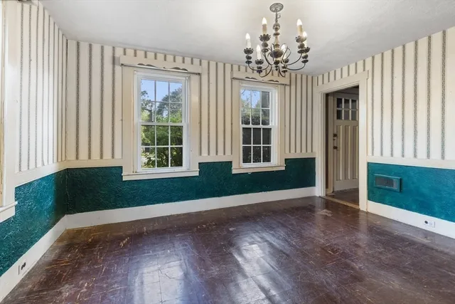 an empty room with wooden floor chandelier and windows