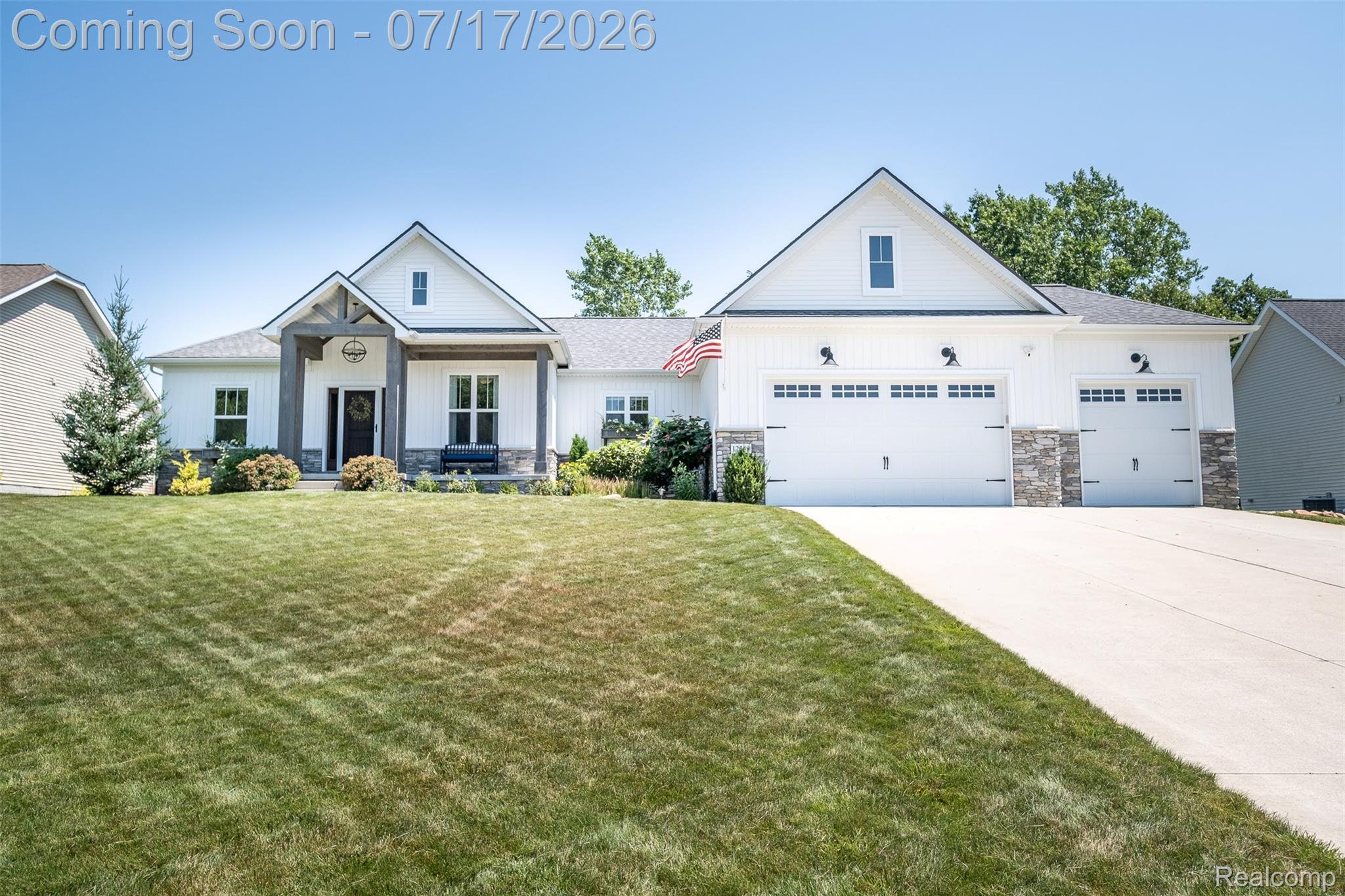 12349 Sugar Maple Drive Fenton, MI 48430 - Photo 2 of 67 Modern farmhouse exterior featuring white vertical and horizontal siding, stone accents, a covered entry with timber-style columns, and a concrete driveway leading to a multi-car garage with carriage-style doors