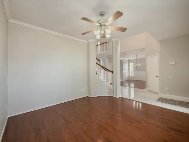 a view of an empty room with wooden floor and a ceiling fan