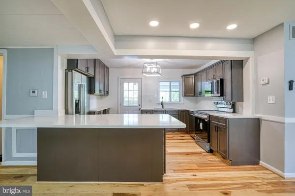 a large kitchen with kitchen island a stove a sink dishwasher and a dining table with wooden floor