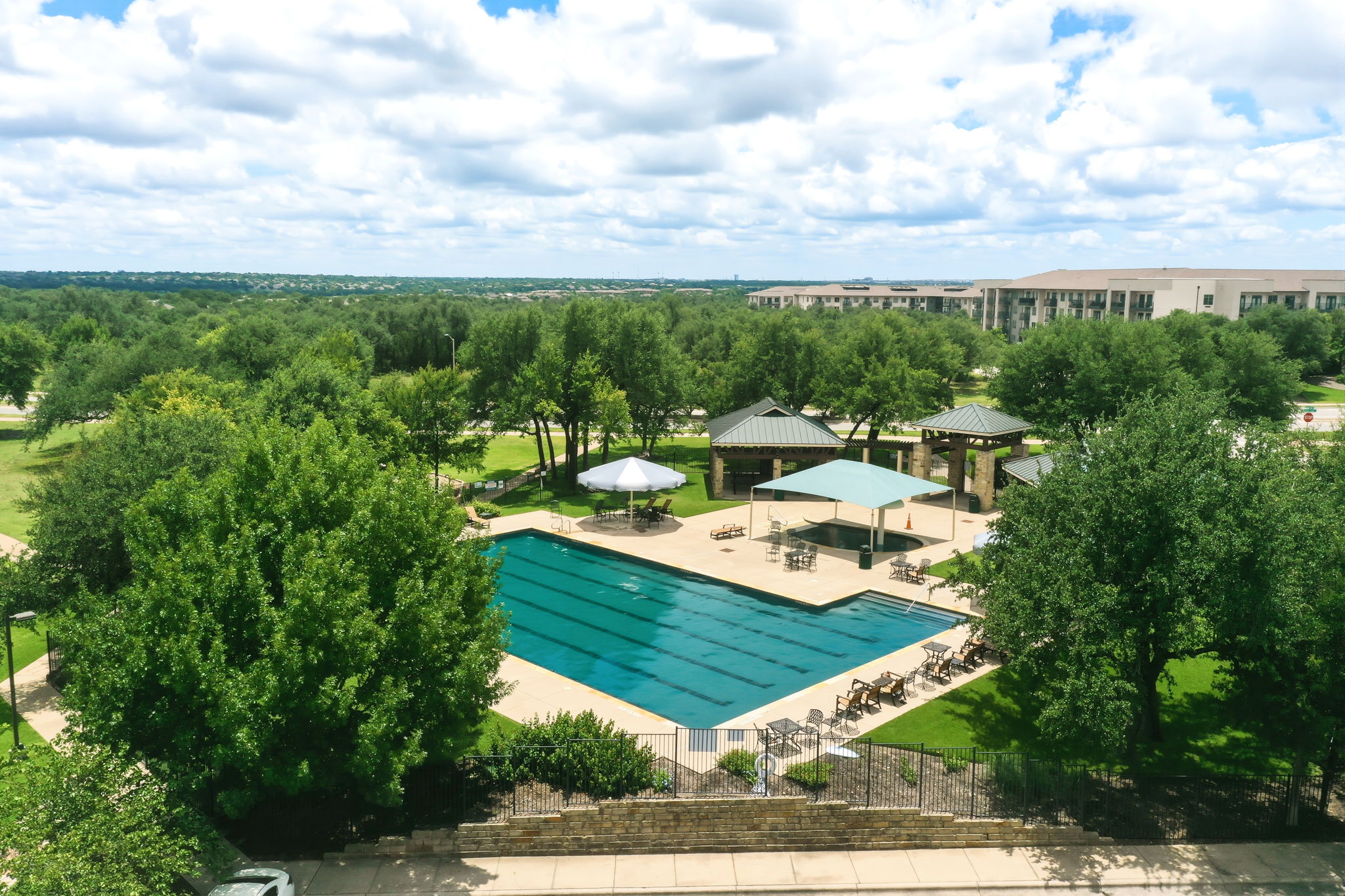 110 Dasher Drive Cedar Park, TX 78613 - Photo 38 of 39 A refreshing outdoor pool with shaded lounge areas awaits, framed by verdant trees and open skies.