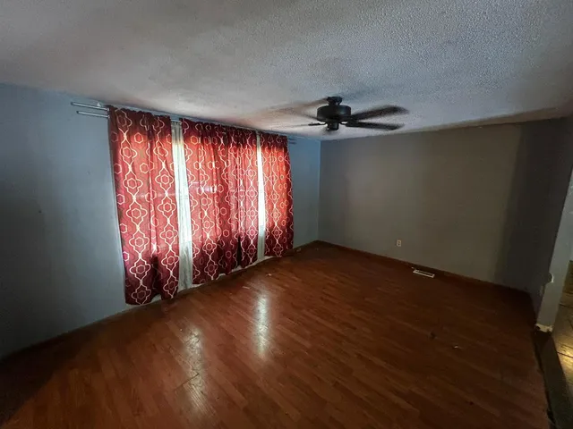 an empty room with wooden floor fan and windows