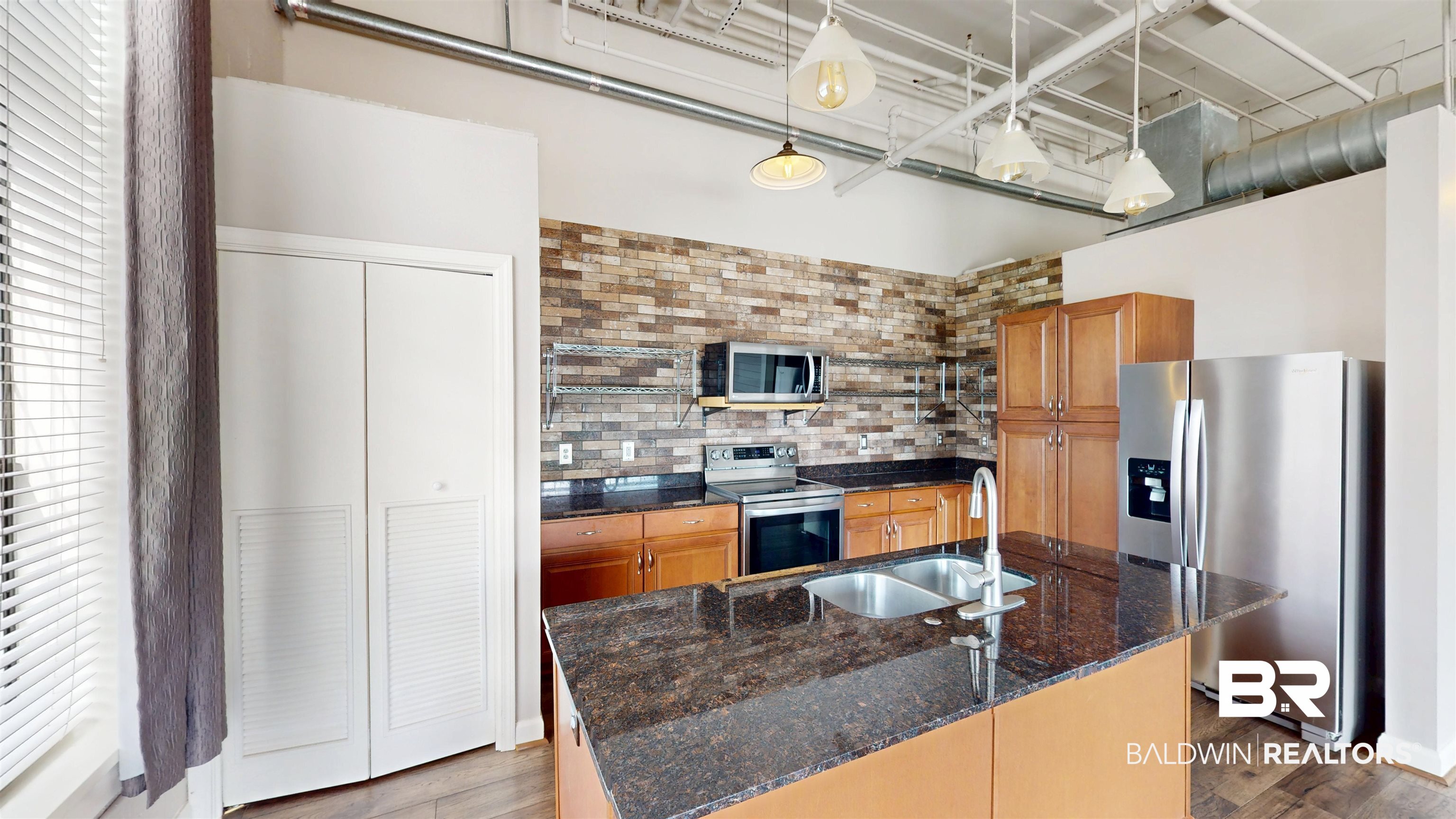 308 St Louis Street, Unit 101 Mobile, AL 36602 - Photo 24 of 30 Kitchen featuring dark stone countertops, appliances with stainless steel finishes, an island with sink, and brown cabinets