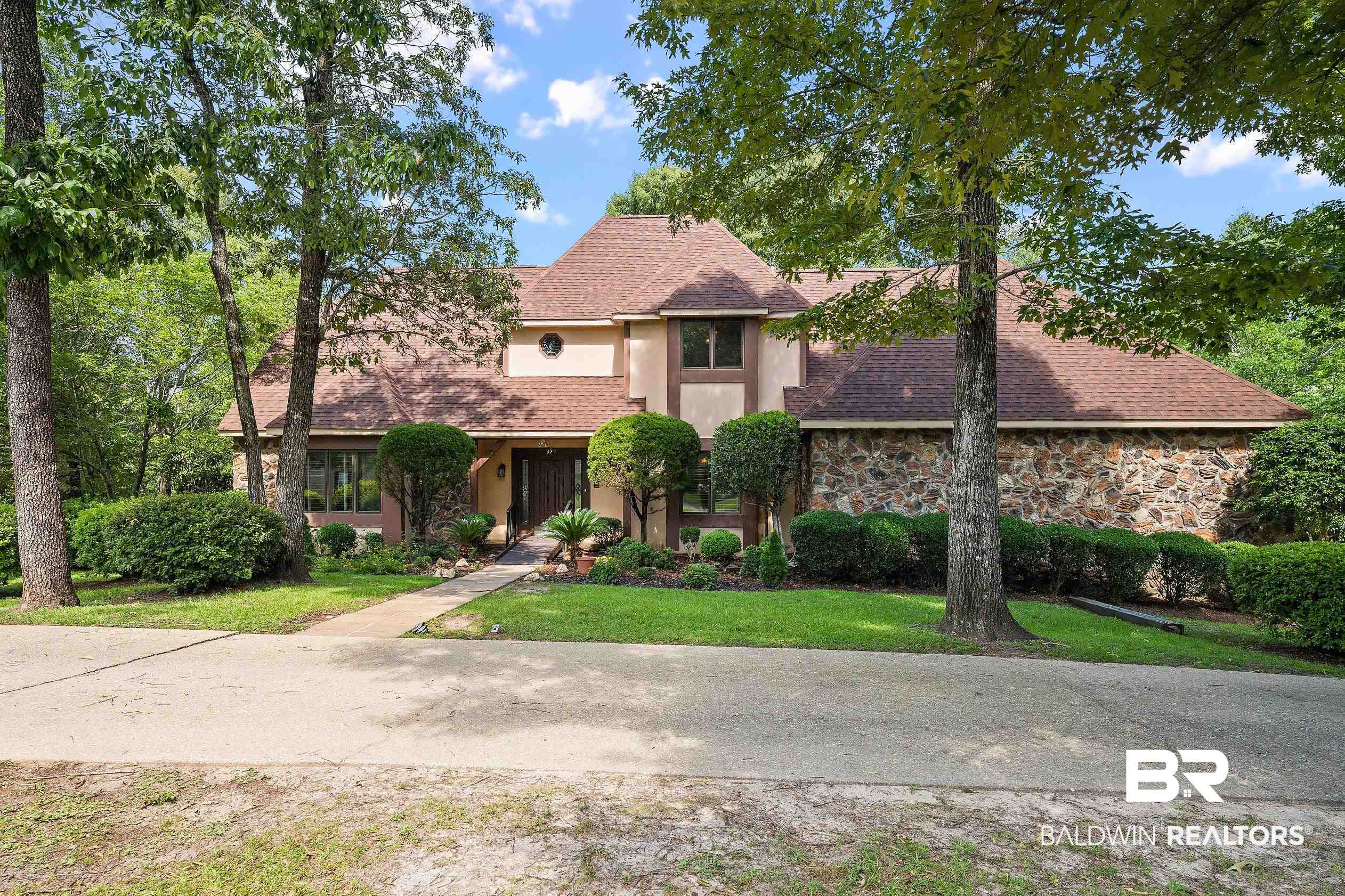 329 Norwood Road Monroeville, AL 36460 - Photo 2 of 49 Stucco and stone exterior featuring a prominent gabled roofline, mature trees, a concrete walkway, and established landscaping