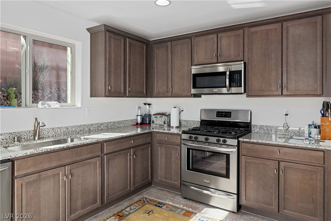 2269 Chandler Ranch Place Laughlin, NV 89029 - Photo 13 of 96 Kitchen featuring stainless steel appliances, light stone counters, dark brown cabinetry, light tile patterned flooring, and recessed lighting