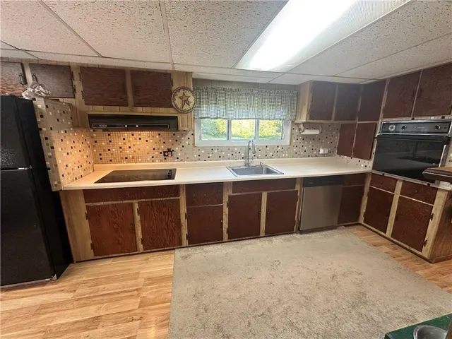 a view of a kitchen with kitchen island a sink wooden floor and black appliances