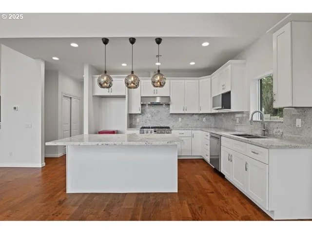 a kitchen with kitchen island granite countertop a sink dishwasher a stove and a dining table with wooden floor