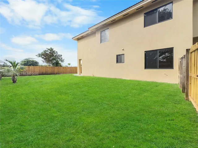 a view of a white house with a small yard and large trees