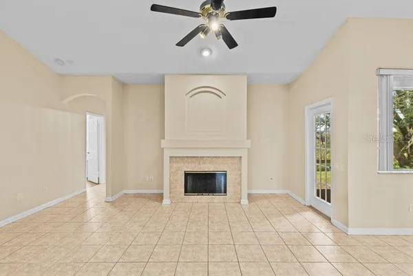 a view of an empty room with chandelier fan and fire place