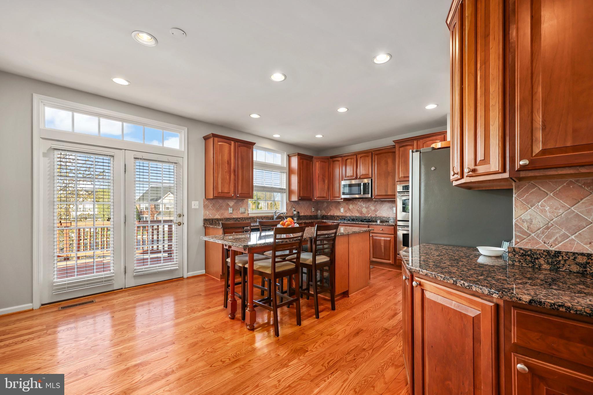 41742 Experience Way Aldie, VA 20105 - Photo 16 of 78 a kitchen with stainless steel appliances granite countertop wooden cabinets a dining table and chairs