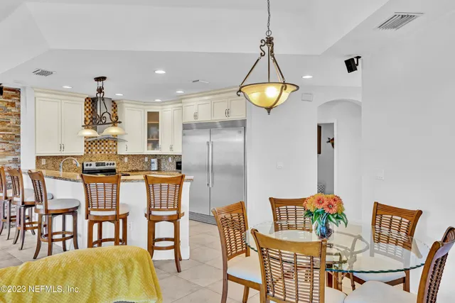 a kitchen with stainless steel appliances kitchen island granite countertop a dining table chairs and a refrigerator