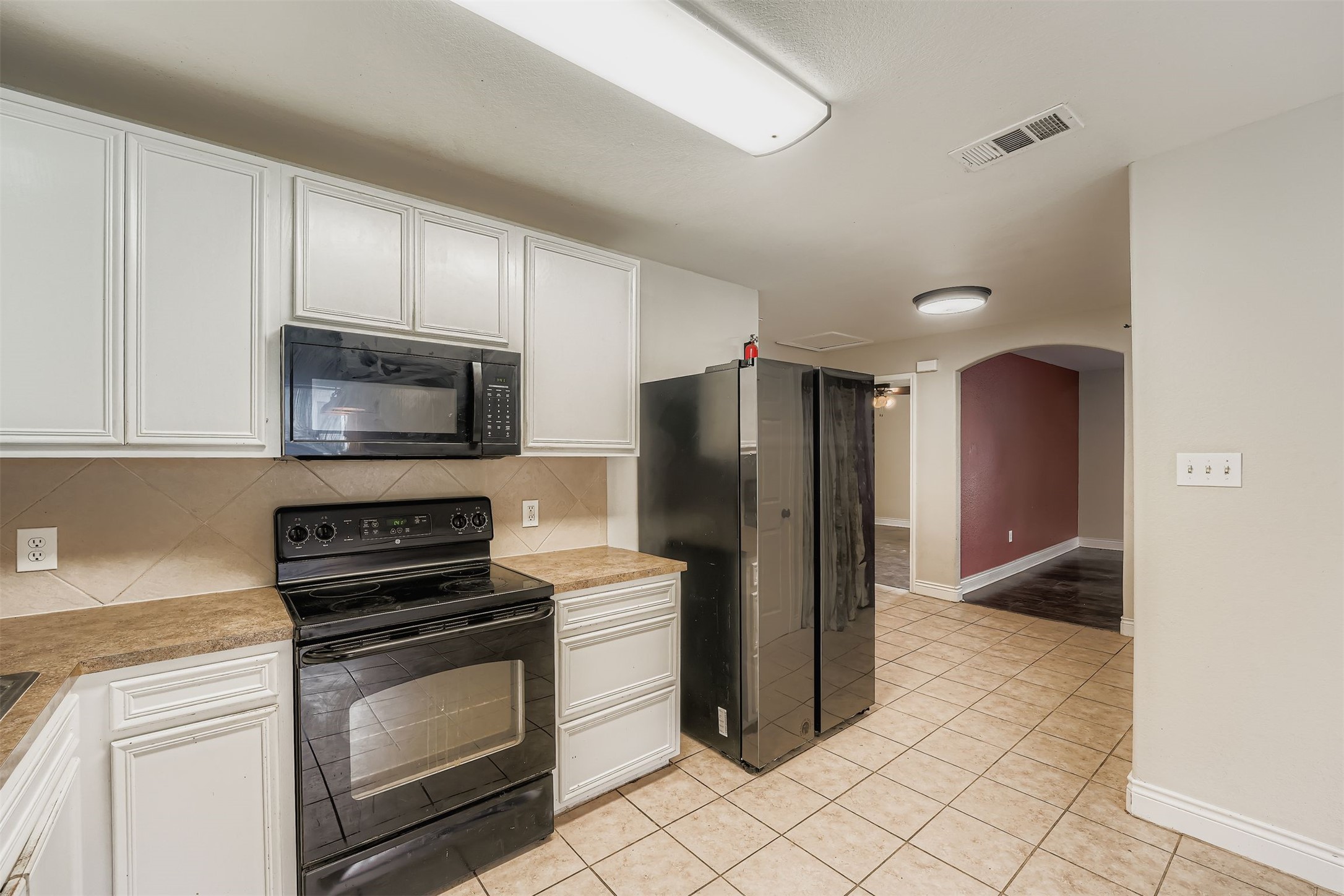 304 South Main Street Elgin, TX 78621 - Photo 14 of 25 Kitchen with black appliances, white cabinetry, light countertops, arched walkways, and decorative backsplash