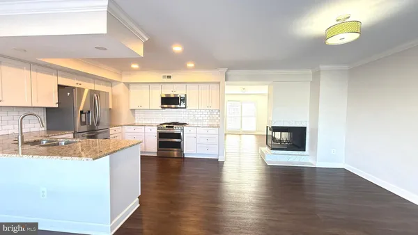 a kitchen with stainless steel appliances granite countertop a stove a sink a refrigerator white cabinets and wooden floor