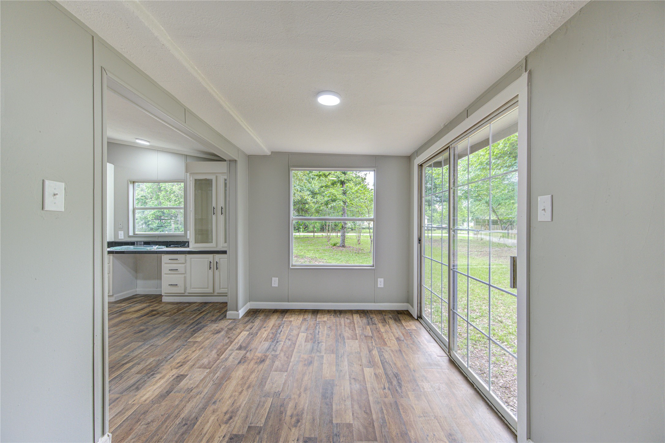 30226 Davis Street Magnolia, TX 77355 - Photo 14 of 50 This bright room features large sliding glass doors and a window offering scenic views of greenery. The space has wood-style flooring and neutral walls, leading into an adjacent room with cabinetry, perfect for dining or a sunroom.