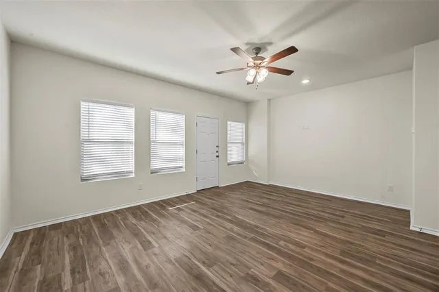 a view of an empty room with chandelier fan and wooden floor