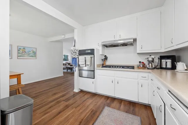 a kitchen with stainless steel appliances granite countertop a sink dishwasher stove and white cabinets with wooden floor