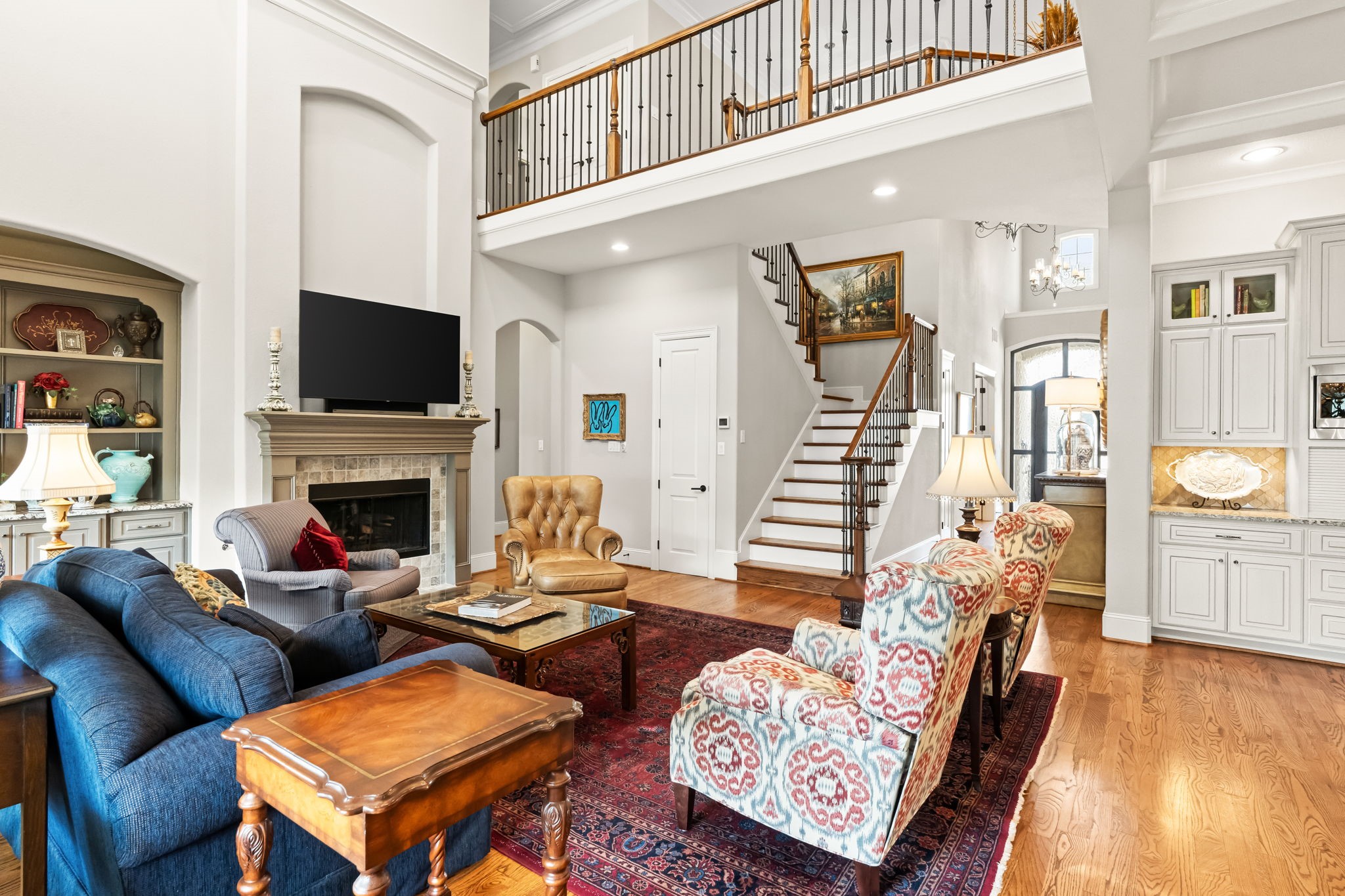 4823 Jason Street Houston, TX 77096 - Photo 11 of 40 This spacious living room boasts high ceilings, a cozy fireplace, and elegant built-in shelving. The open layout includes a stylish staircase and a blend of classic and modern furnishings, creating a warm and inviting atmosphere.