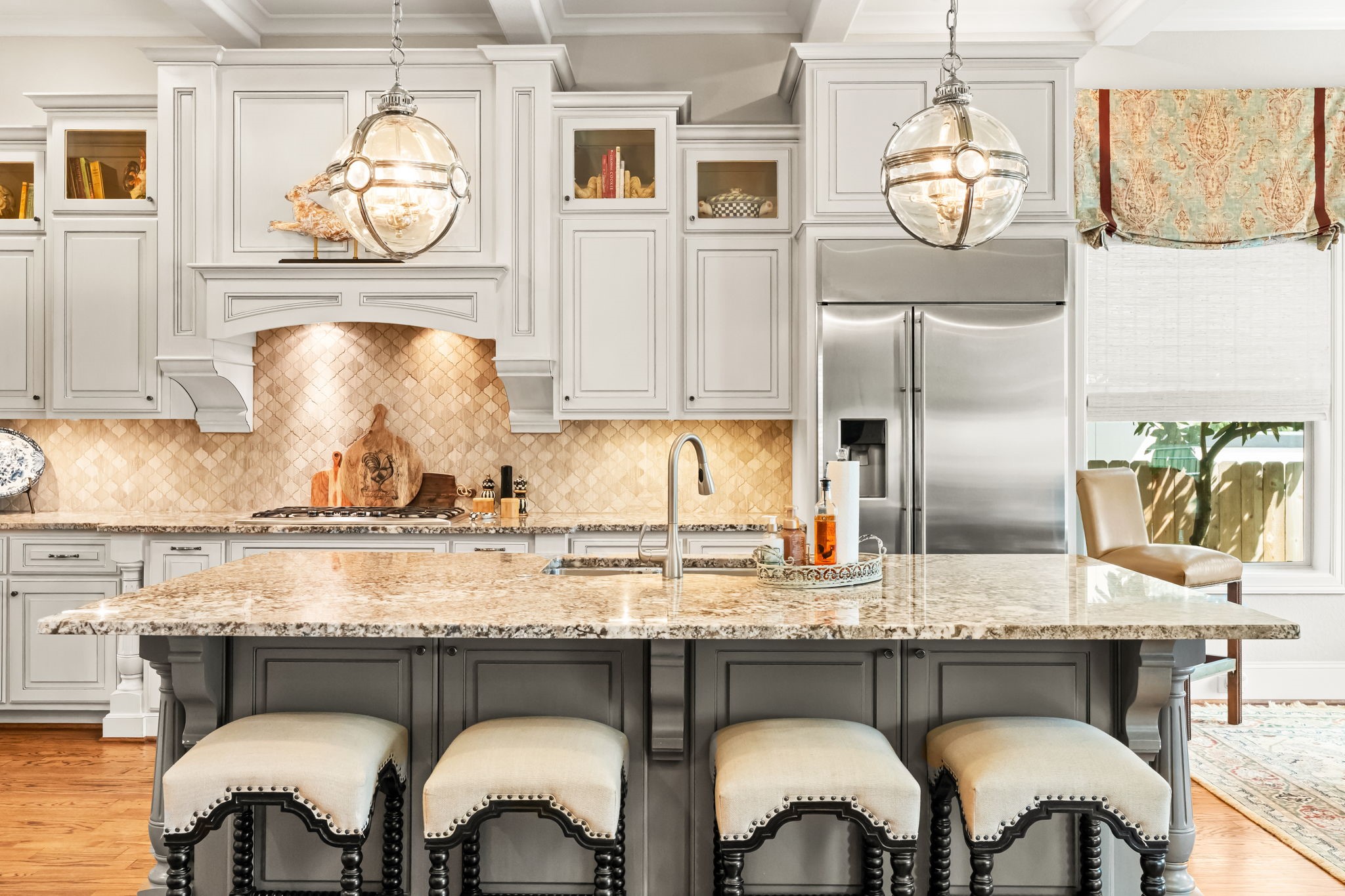 4823 Jason Street Houston, TX 77096 - Photo 12 of 40 This kitchen features elegant cabinetry with glass accents, a spacious granite island with seating, stainless steel appliances, and stylish pendant lighting. The warm wood flooring and neutral backsplash create a cozy, inviting atmosphere.