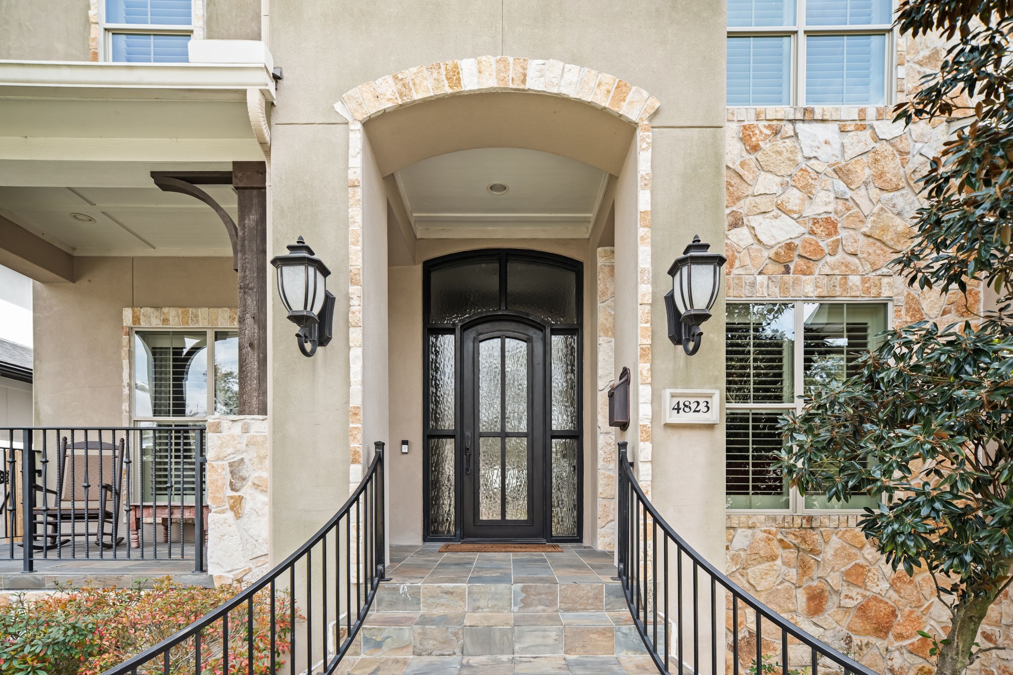 4823 Jason Street Houston, TX 77096 - Photo 3 of 40 This inviting entrance features a stone facade and elegant glass front doors, framed by stylish wall lanterns. The arched doorway and wrought iron railing add charm, while the porch offers a cozy spot to relax.