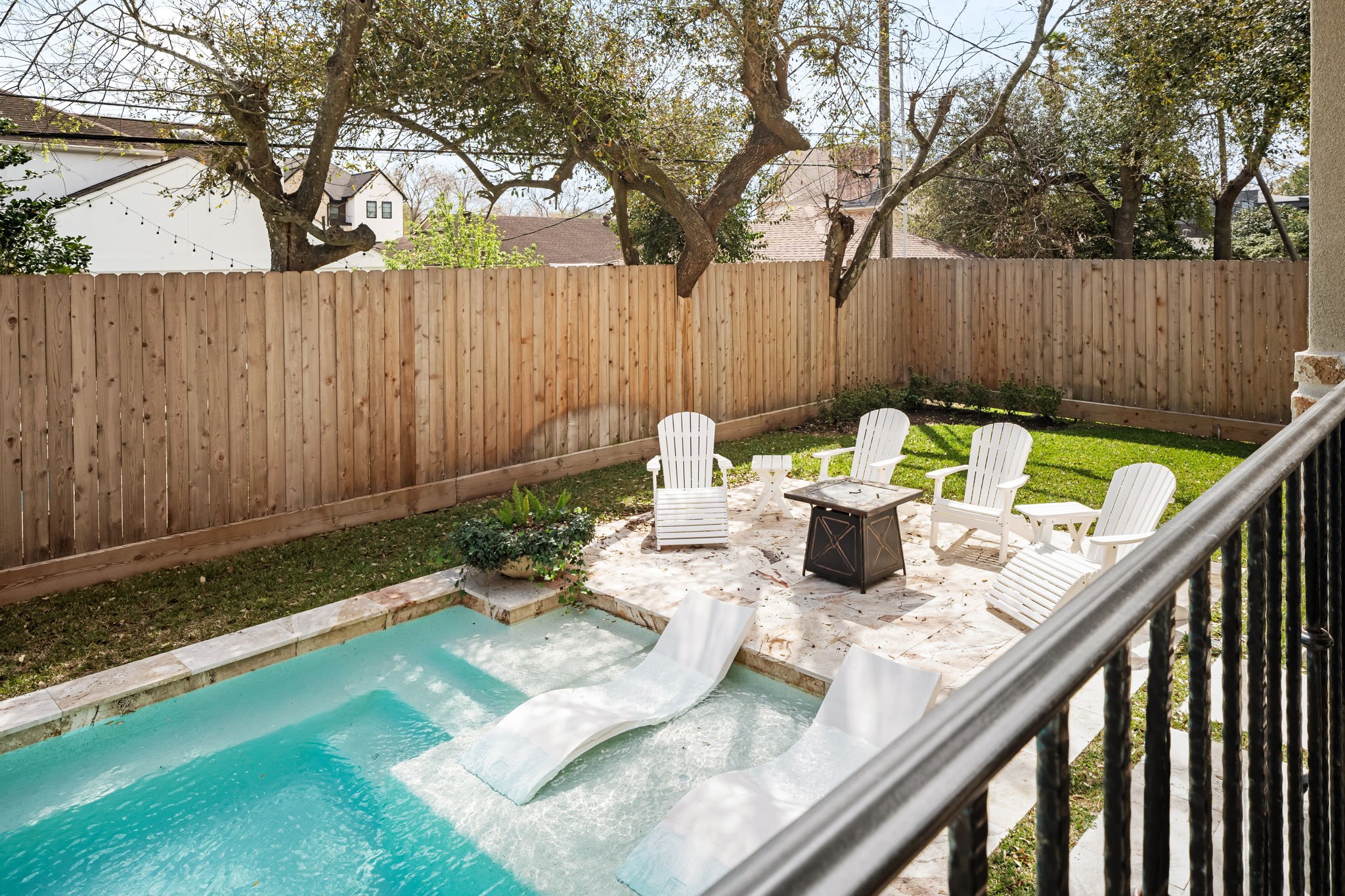 4823 Jason Street Houston, TX 77096 - Photo 37 of 40 This backyard features a private pool with in-water loungers, a patio area with Adirondack chairs, a fire pit, and lush greenery, all enclosed by a wooden fence for privacy.