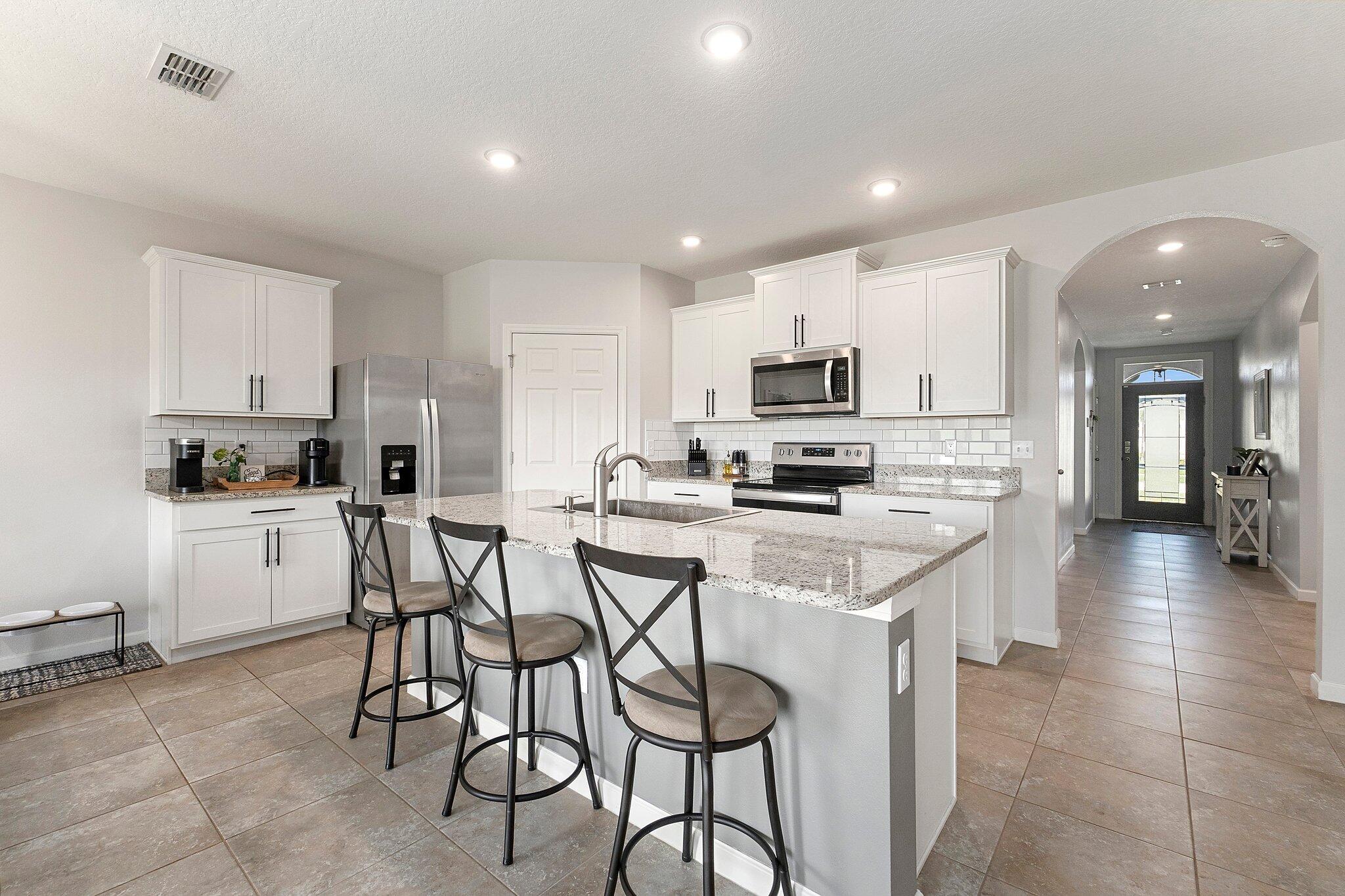 10850 Pacini Way Port St. Lucie, FL 34987 - Photo 9 of 36 a kitchen with stainless steel appliances kitchen island granite countertop a stove a sink a refrigerator and white cabinets with wooden floor