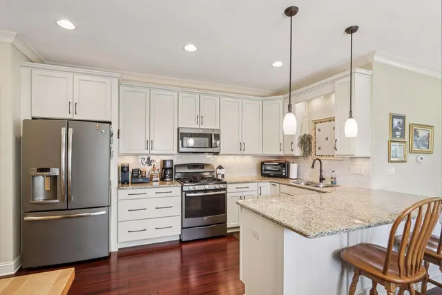 a kitchen with granite countertop a refrigerator a stove a sink and white cabinets with wooden floor