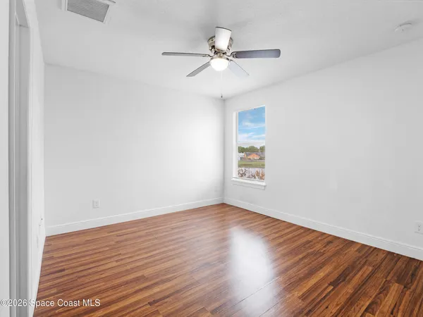 an empty room with wooden floor fan and windows