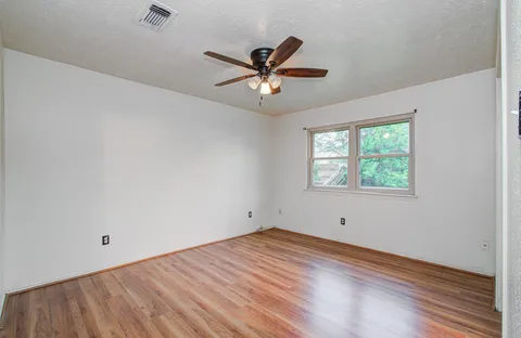 a view of empty room with wooden floor and fan