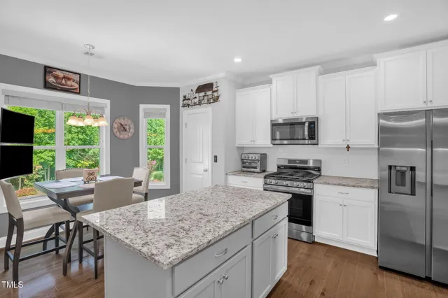 a kitchen with stainless steel appliances granite countertop a stove top oven a sink dishwasher a refrigerator and a dining table with wooden floor
