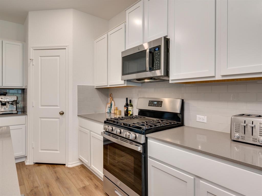 1208 Sweetspire Street Leander, TX 78641 - Photo 7 of 36 Kitchen featuring white shaker cabinetry, stainless steel appliances, gray subway tile backsplash, light wood-finish flooring, and light gray countertops