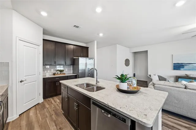 a kitchen with stainless steel appliances granite countertop a stove top oven a sink dishwasher a dining table and chairs with wooden floor