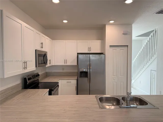 a kitchen with stainless steel appliances kitchen island granite countertop a refrigerator a stove a sink and white cabinets with wooden floor