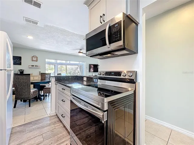 a kitchen with granite countertop a refrigerator a sink dishwasher a stove and white countertops with wooden floor